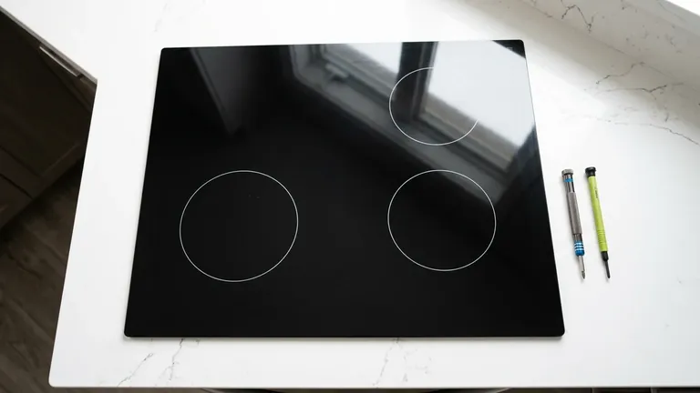 Black smooth-glass induction cooktop with small service tools nearby
